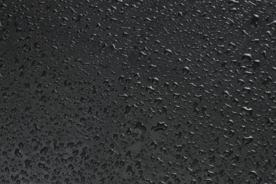 Photo of Water drops on dark grey glass surface, top view