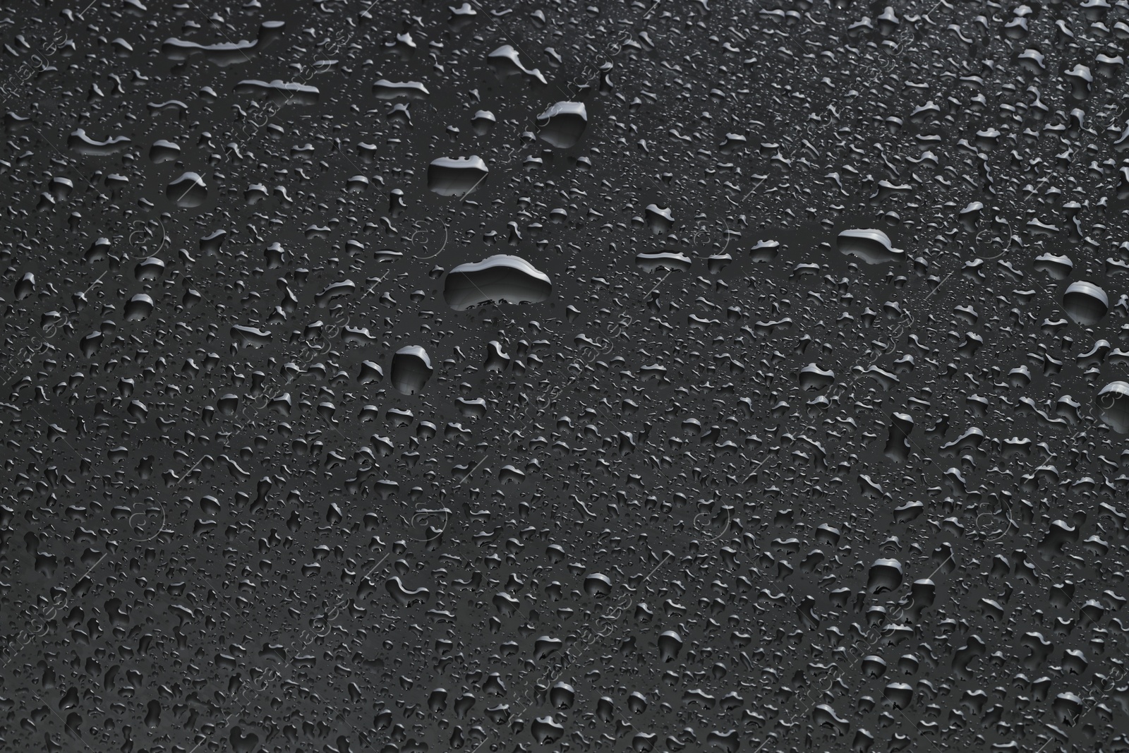 Photo of Water drops on dark grey glass surface, top view