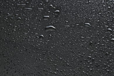 Photo of Water drops on dark grey glass surface, top view