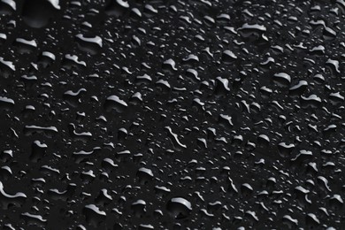 Photo of Water drops on black glass surface, closeup