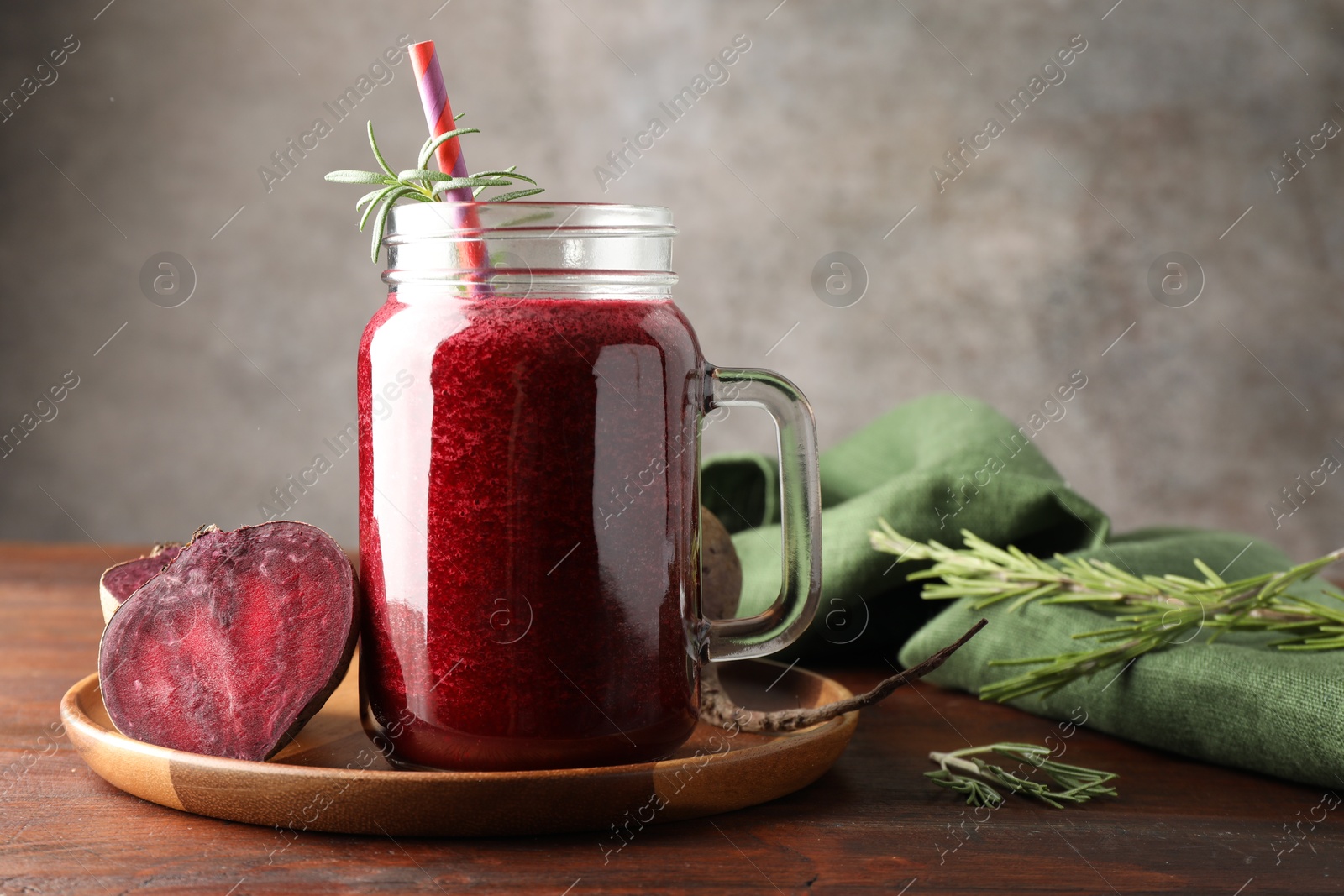 Photo of Fresh beetroot smoothie in mason jar, rosemary and vegetables on wooden table, closeup