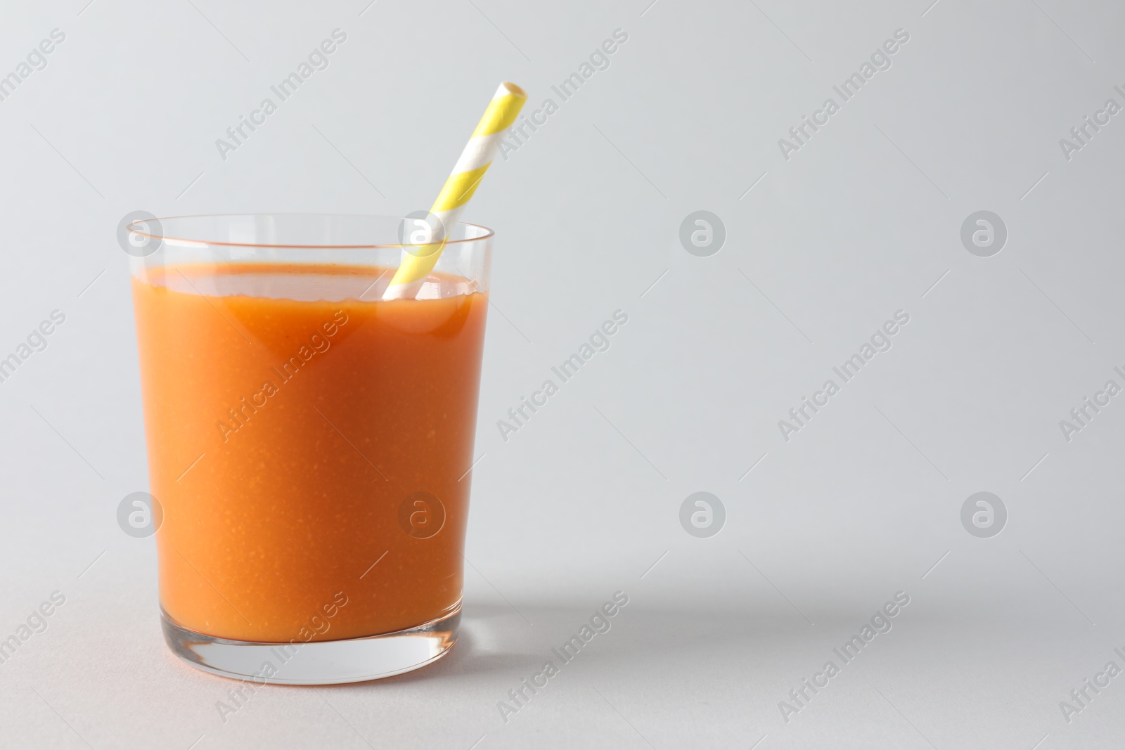 Photo of Fresh carrot smoothie in glass on light grey background, closeup. Space for text