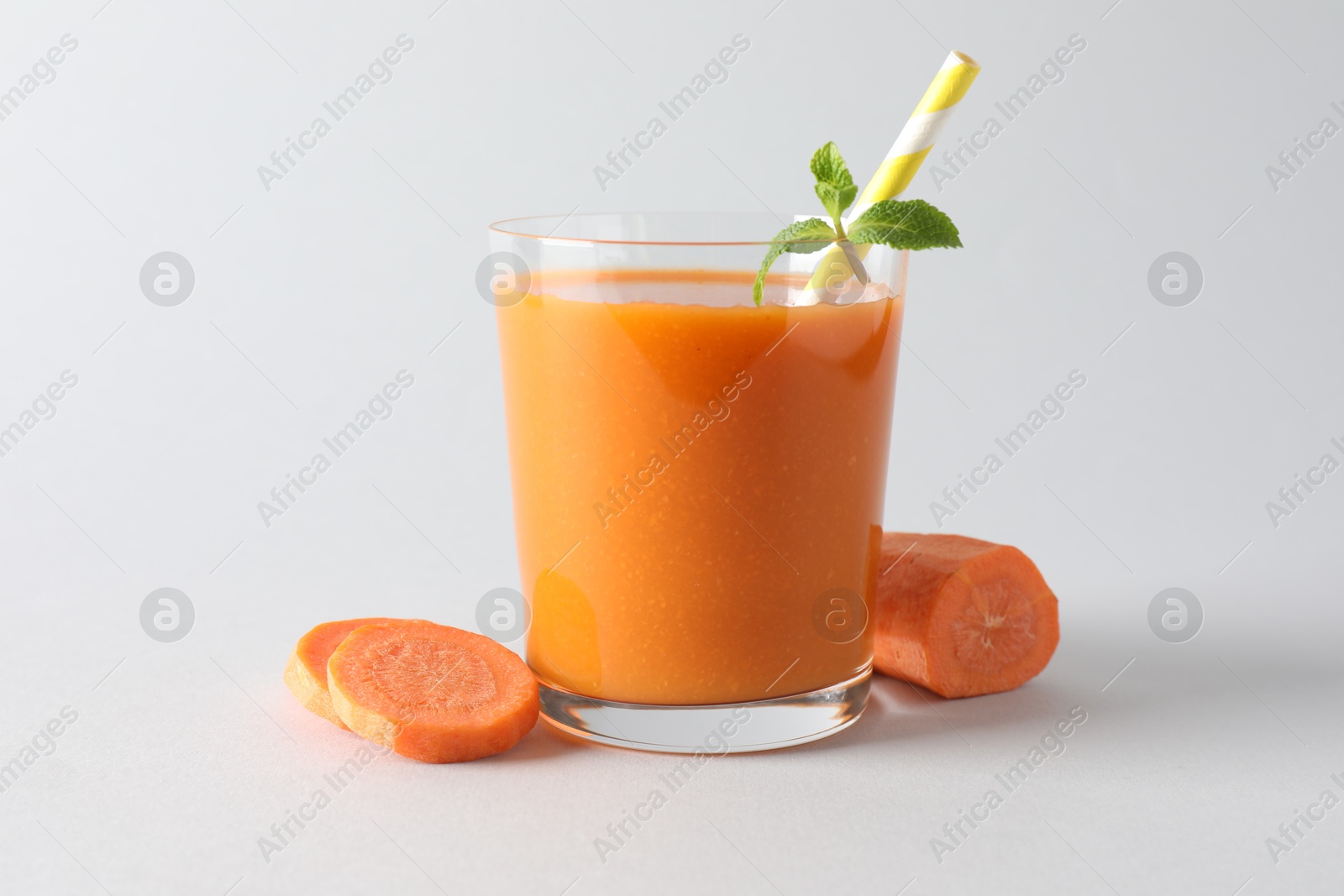 Photo of Fresh carrot smoothie in glass and cut vegetable on light grey background, closeup