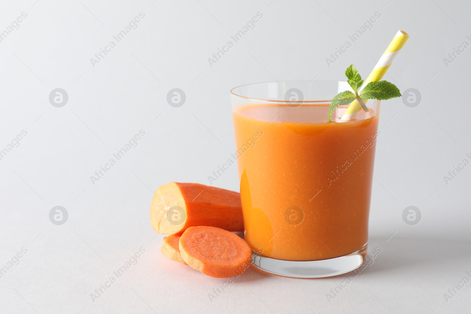 Photo of Fresh carrot smoothie in glass and cut vegetable on light grey background, closeup. Space for text