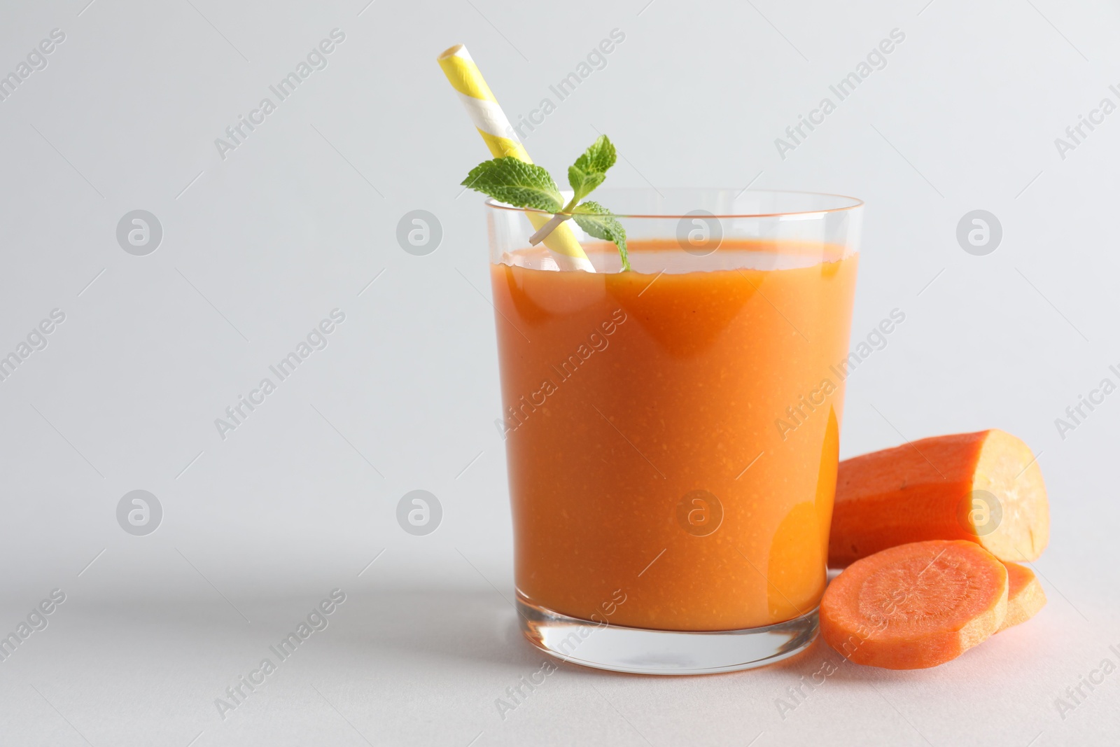 Photo of Fresh carrot smoothie in glass and cut vegetable on light grey background, closeup. Space for text