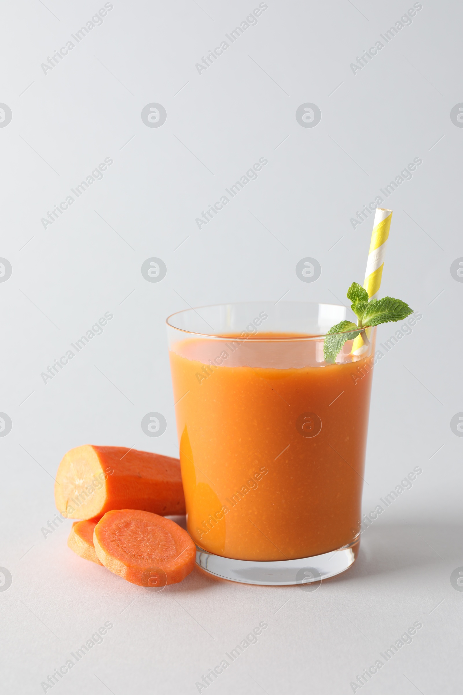 Photo of Fresh carrot smoothie in glass and cut vegetable on light grey background