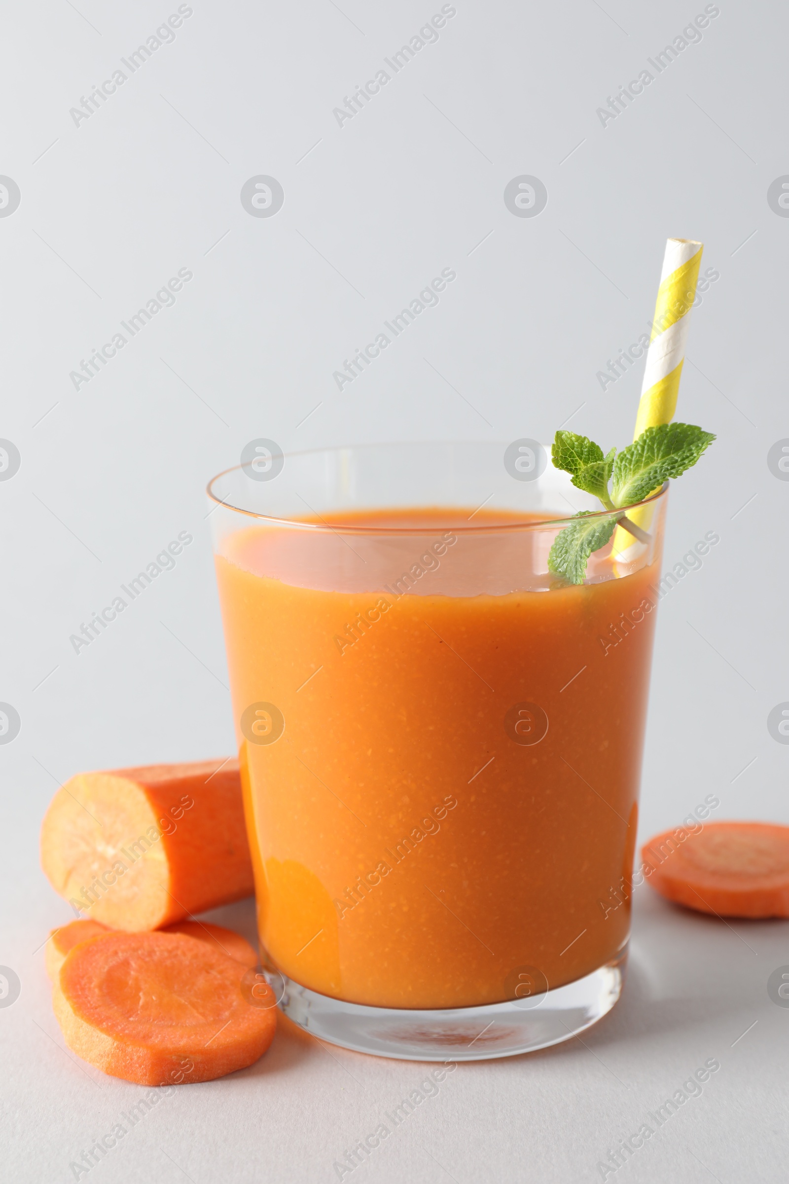 Photo of Fresh carrot smoothie in glass and cut vegetable on light grey background, closeup