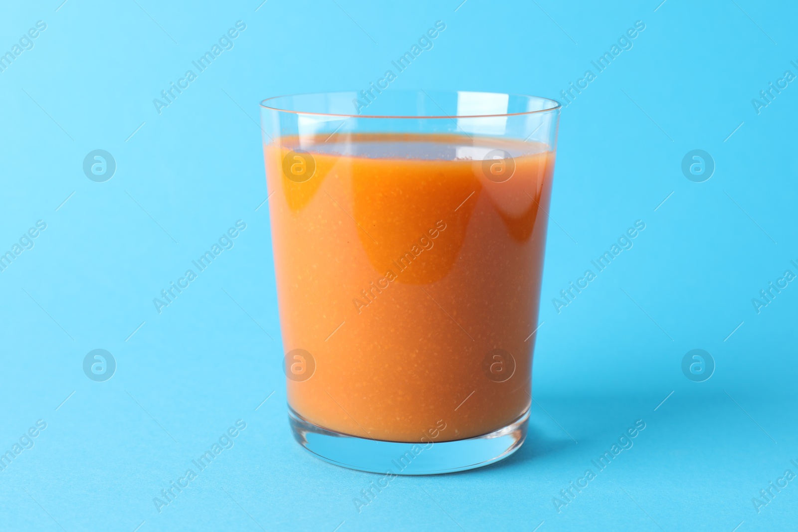 Photo of Fresh carrot smoothie in glass on light blue background, closeup