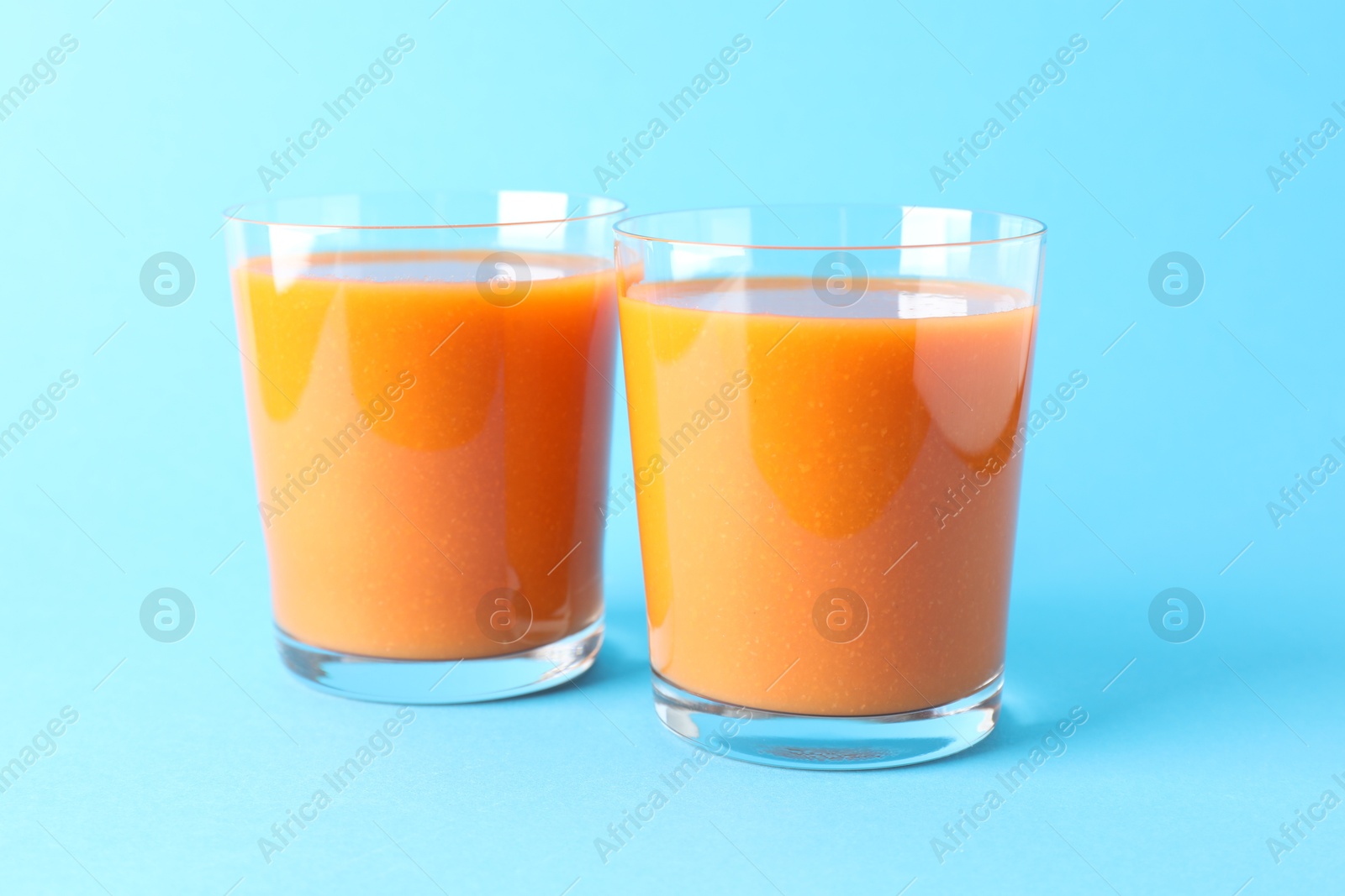 Photo of Fresh carrot smoothie in glasses on light blue background, closeup