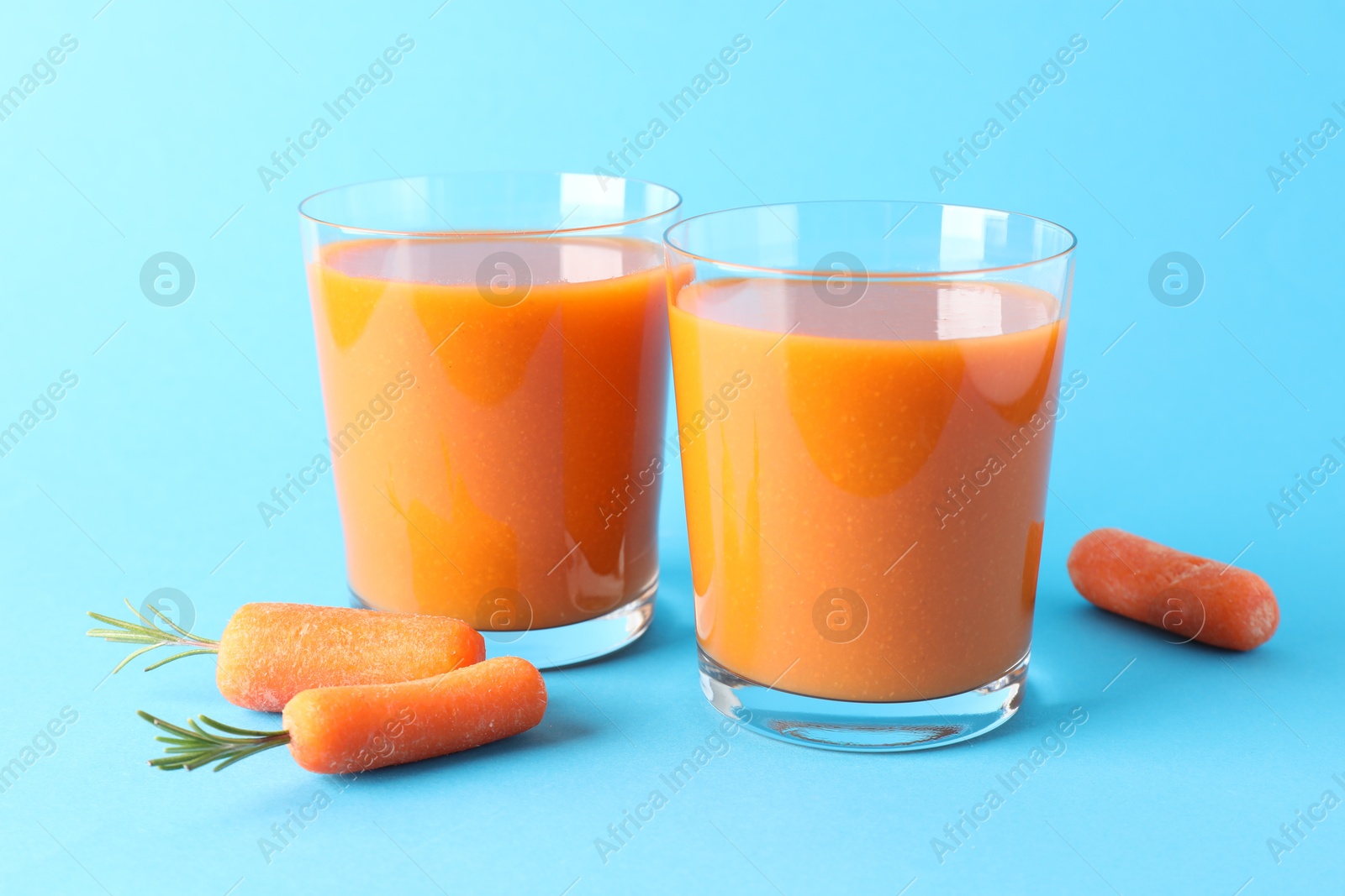 Photo of Fresh carrot smoothie in glasses and vegetables on light blue background, closeup