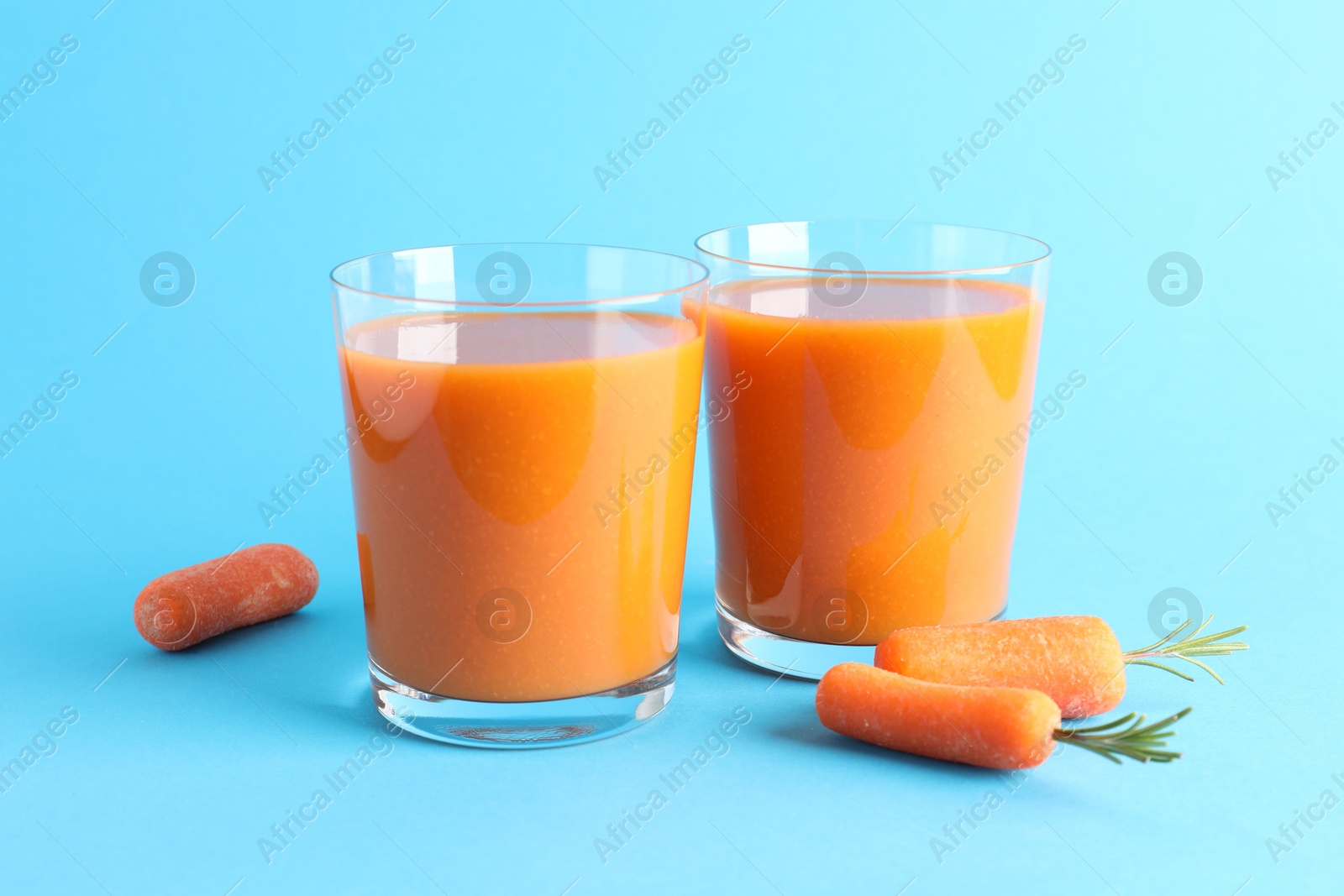 Photo of Fresh carrot smoothie in glasses and vegetables on light blue background, closeup