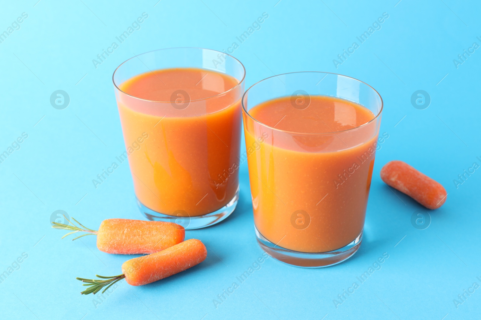 Photo of Fresh carrot smoothie in glasses and vegetables on light blue background, closeup