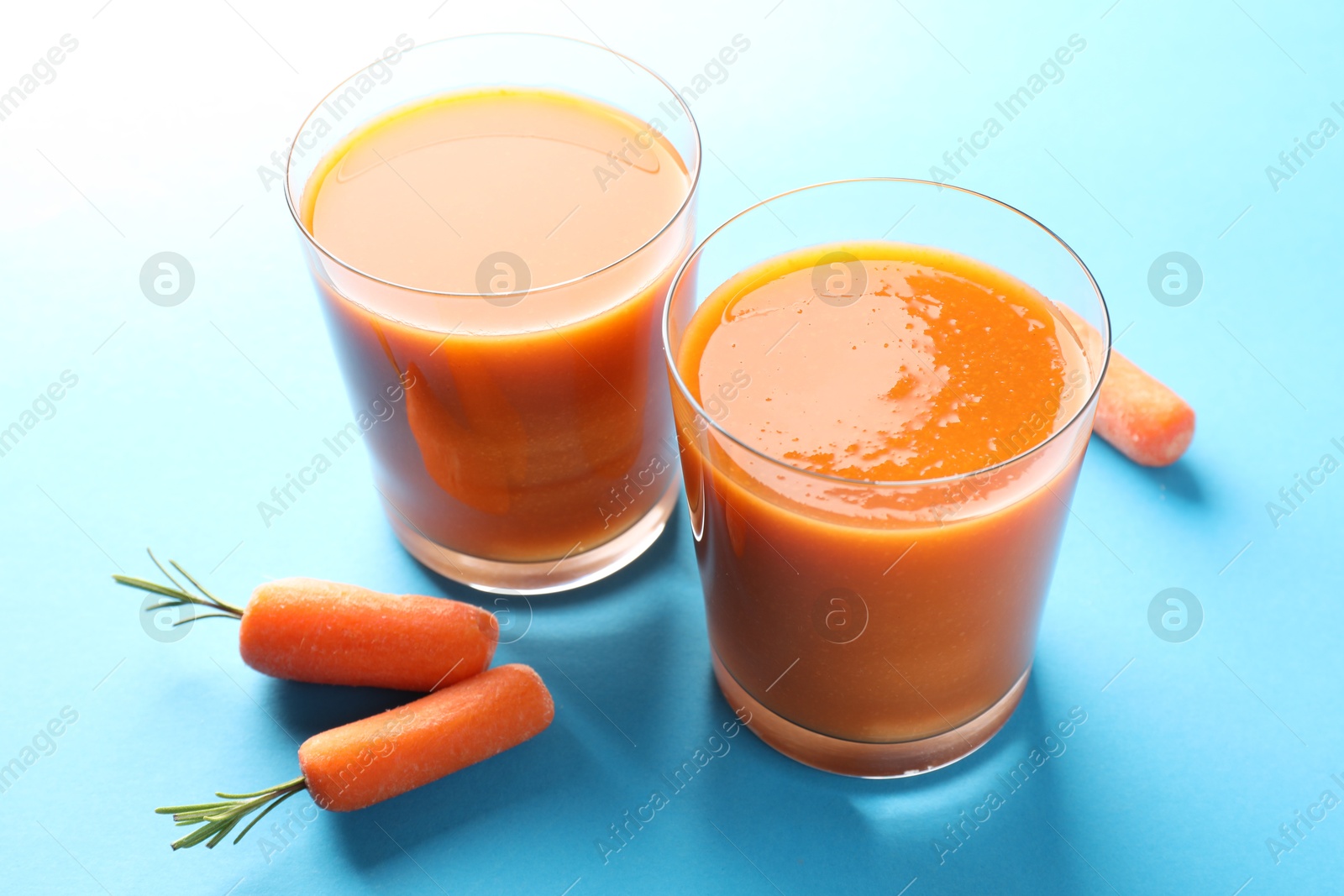 Photo of Fresh carrot smoothie in glasses and vegetables on light blue background, closeup