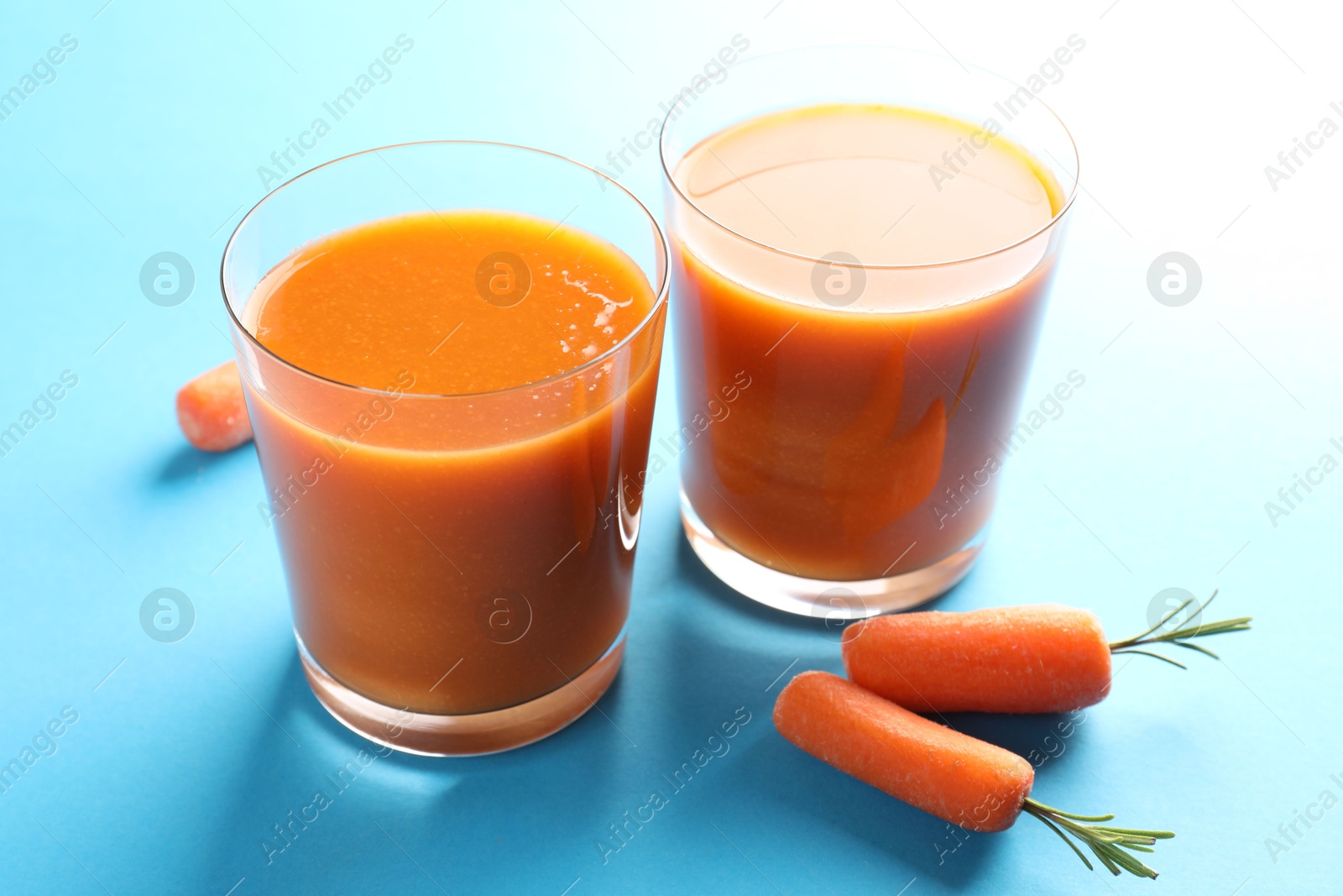 Photo of Fresh carrot smoothie in glasses and vegetables on light blue background, closeup