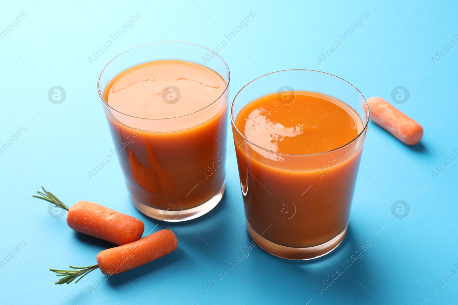 Photo of Fresh carrot smoothie in glasses and vegetables on light blue background, closeup