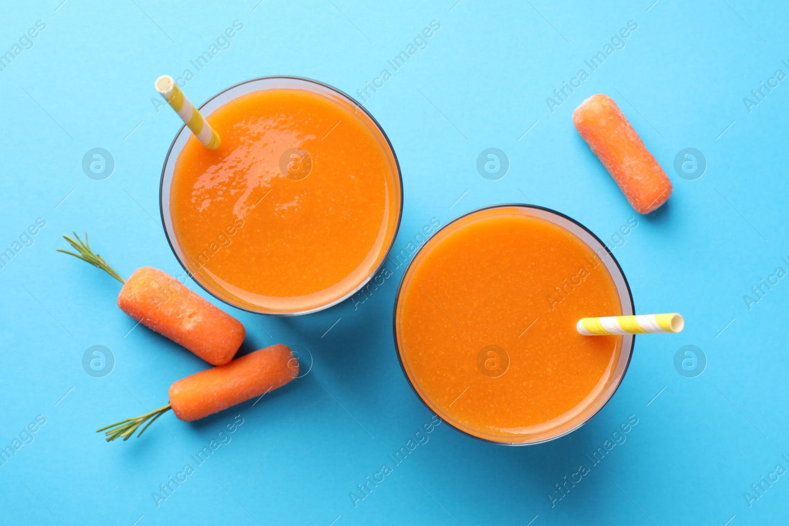 Photo of Fresh carrot smoothie in glasses and vegetables on light blue background, flat lay