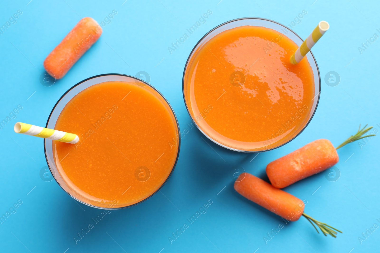 Photo of Fresh carrot smoothie in glasses and vegetables on light blue background, flat lay