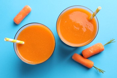 Photo of Fresh carrot smoothie in glasses and vegetables on light blue background, flat lay