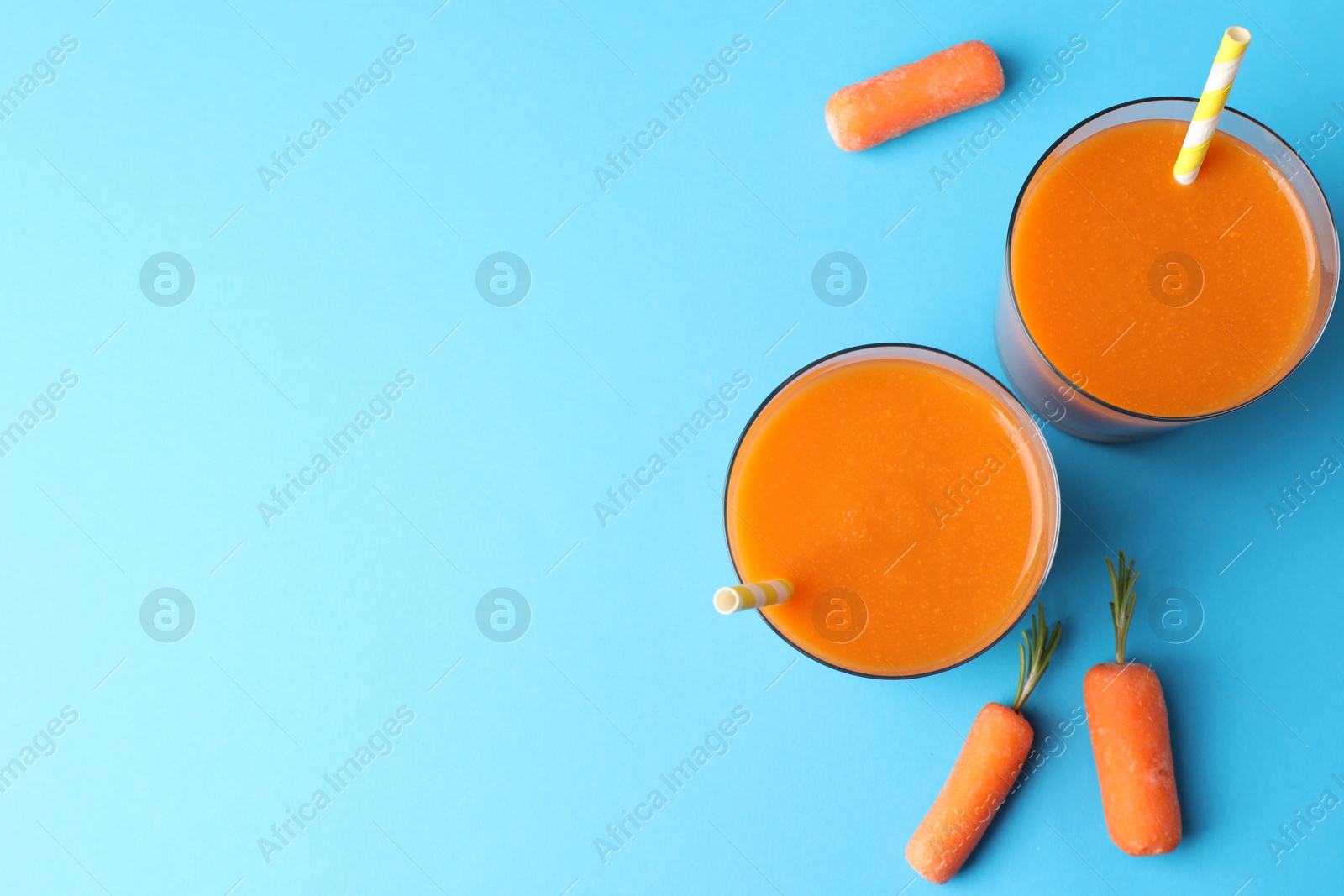 Photo of Fresh carrot smoothie in glasses and vegetables on light blue background, flat lay. Space for text