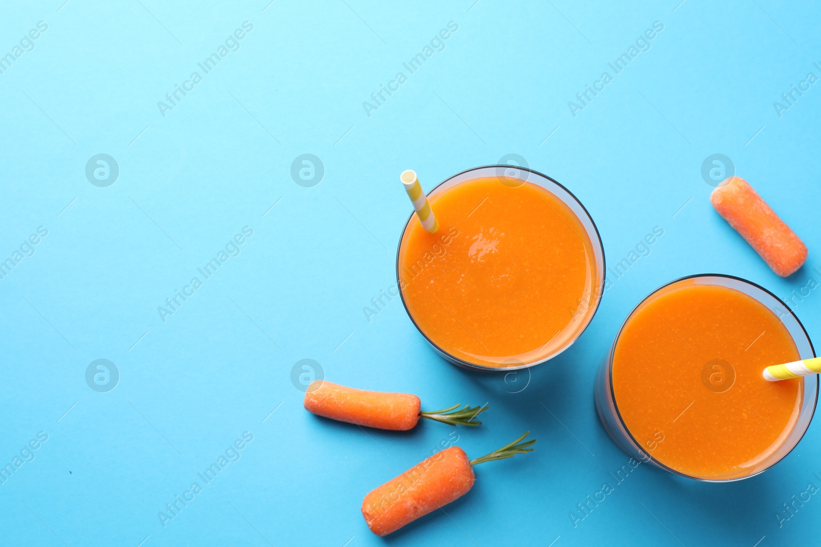 Photo of Fresh carrot smoothie in glasses and vegetables on light blue background, flat lay. Space for text