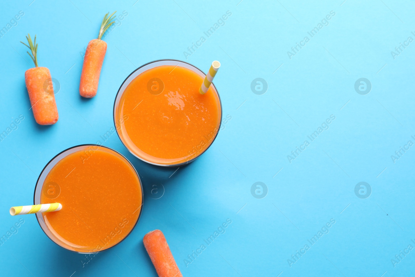 Photo of Fresh carrot smoothie in glasses and vegetables on light blue background, flat lay. Space for text