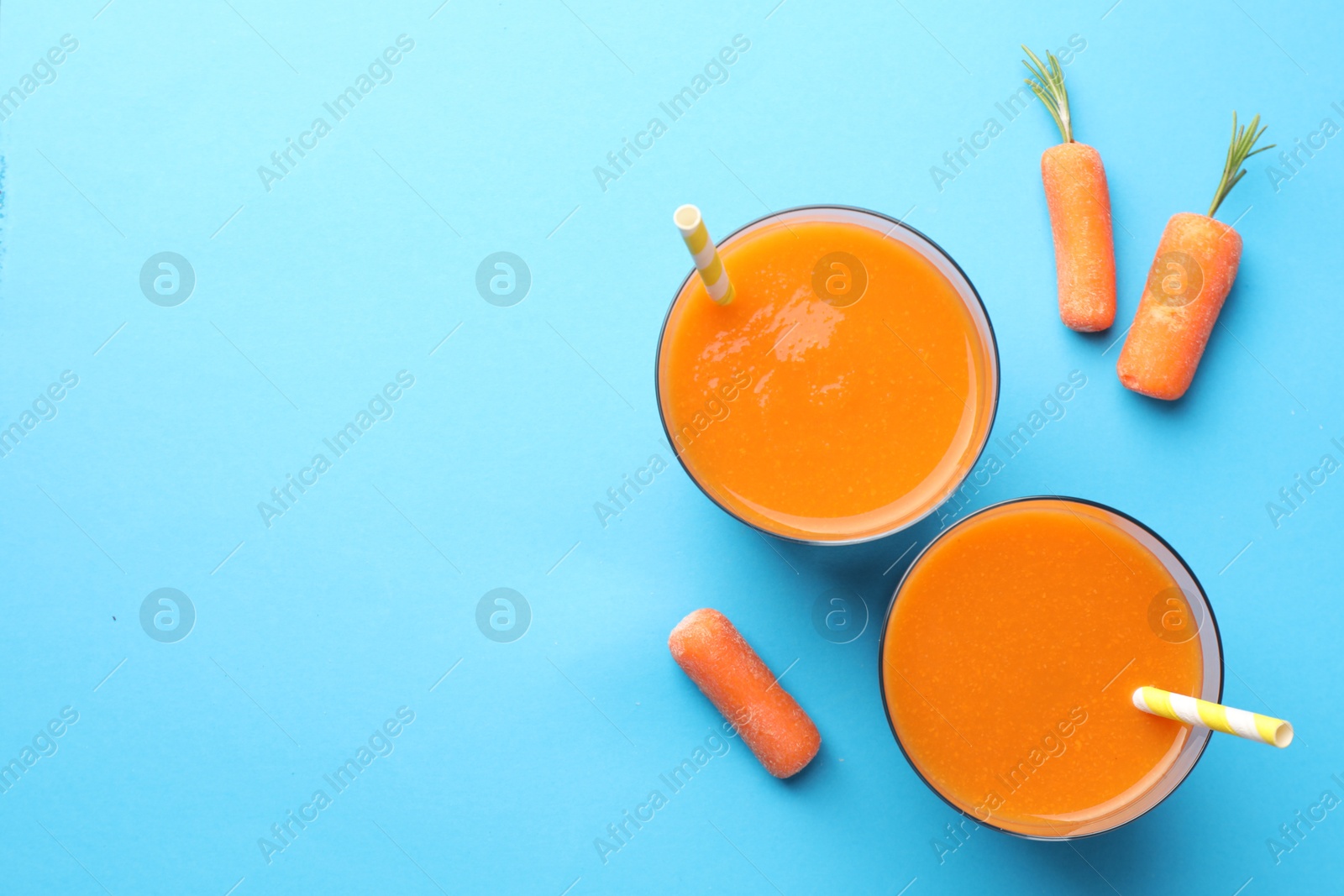 Photo of Fresh carrot smoothie in glasses and vegetables on light blue background, flat lay. Space for text