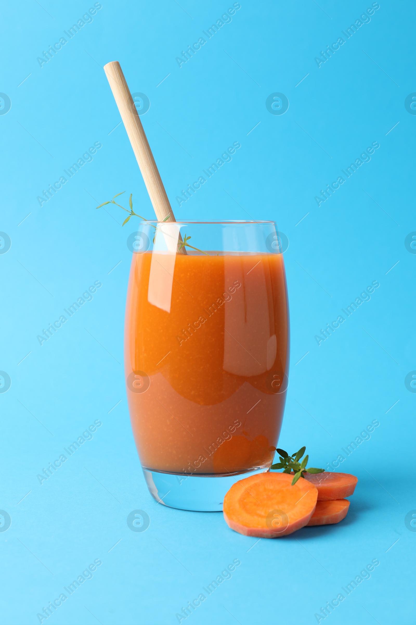 Photo of Fresh carrot smoothie in glass and cut vegetable on light blue background