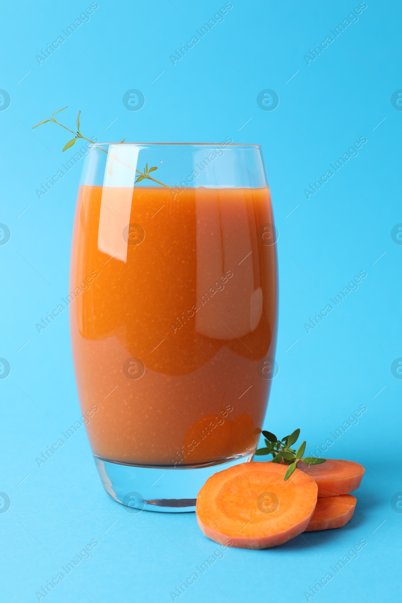 Photo of Fresh carrot smoothie in glass and cut vegetable on light blue background, closeup