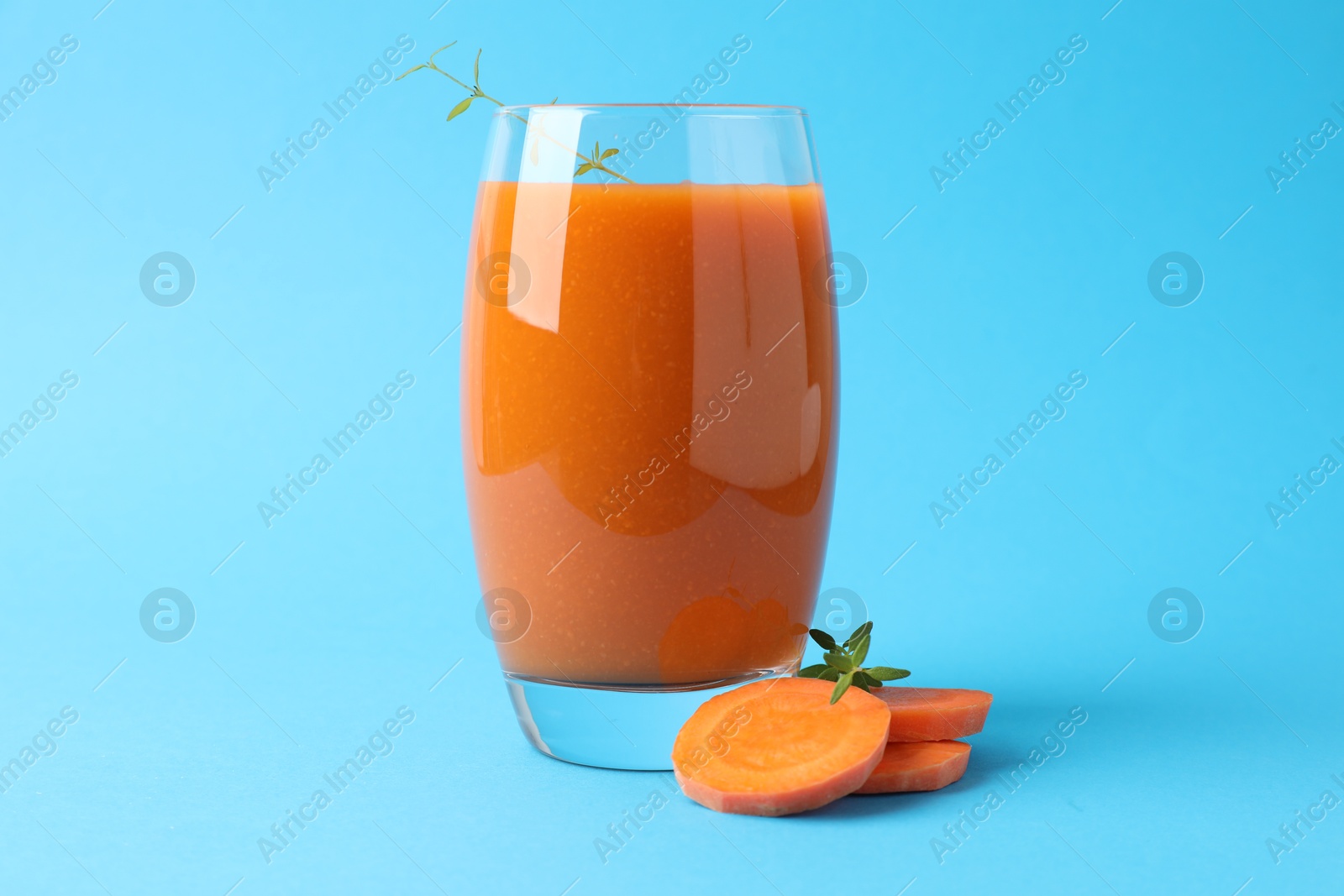 Photo of Fresh carrot smoothie in glass and cut vegetable on light blue background, closeup