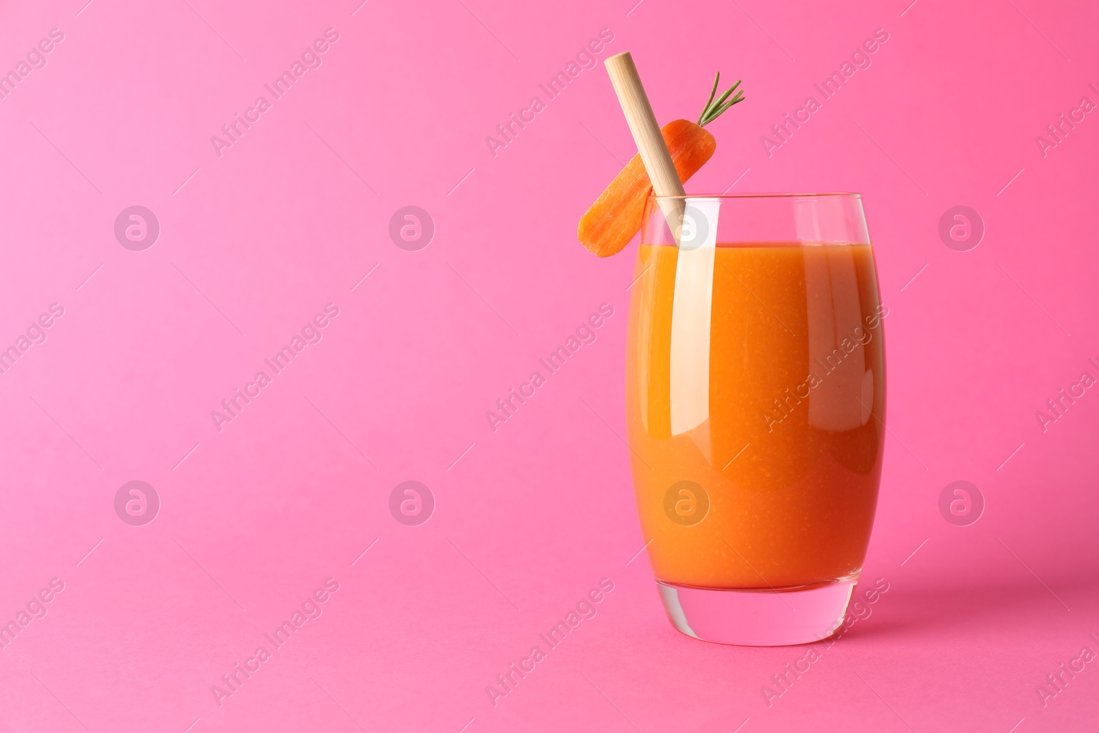 Photo of Fresh carrot smoothie in glass on pink background, closeup. Space for text