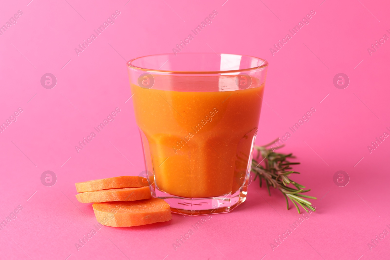 Photo of Fresh carrot smoothie in glass, rosemary and cut vegetable on pink background, closeup