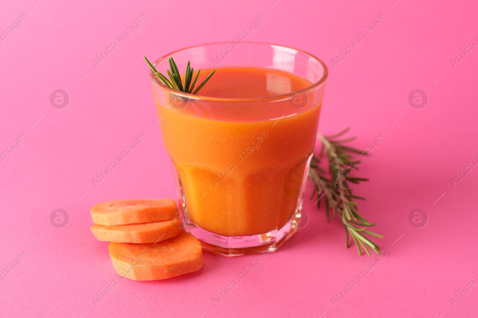 Photo of Fresh carrot smoothie in glass, rosemary and cut vegetable on pink background, closeup