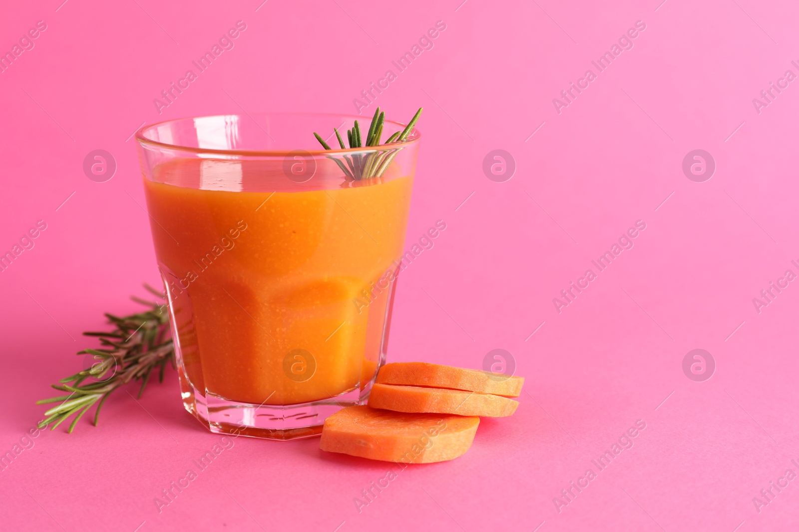 Photo of Fresh carrot smoothie in glass, rosemary and cut vegetable on pink background, closeup. Space for text