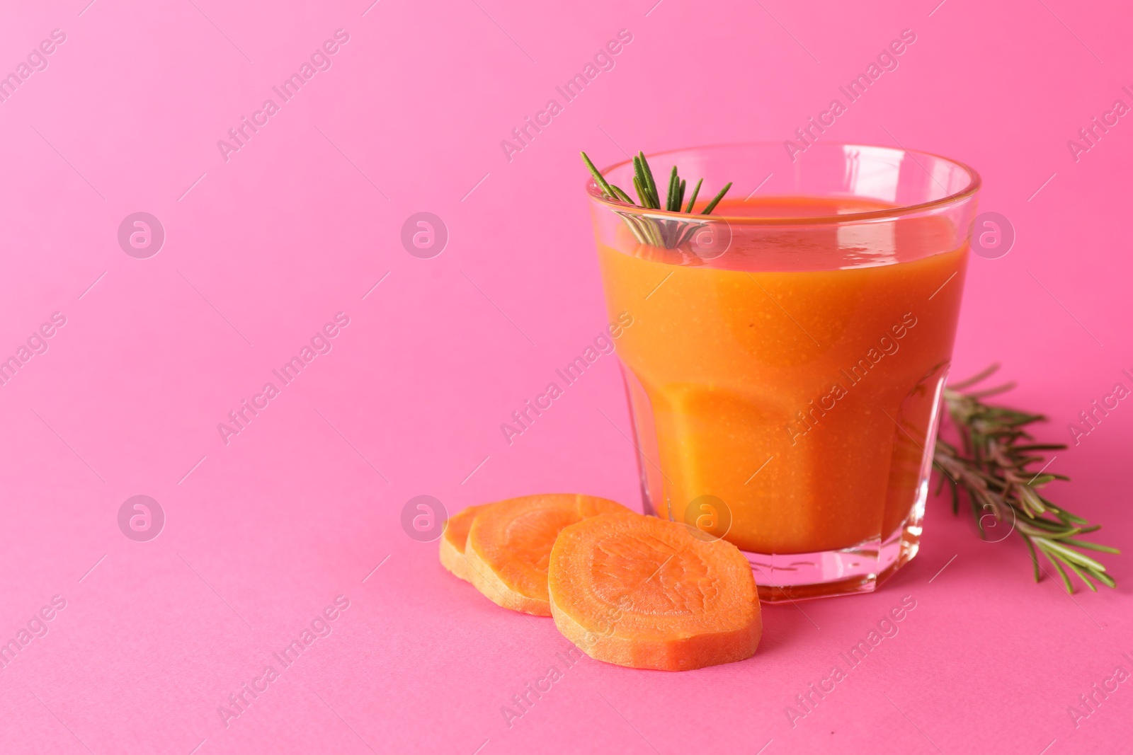 Photo of Fresh carrot smoothie in glass, rosemary and cut vegetable on pink background, closeup. Space for text