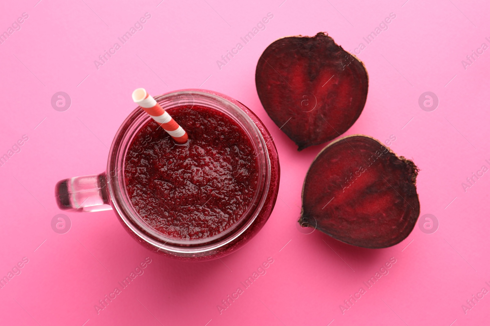 Photo of Fresh beetroot smoothie in mason jar and halves of vegetable on pink background, flat lay