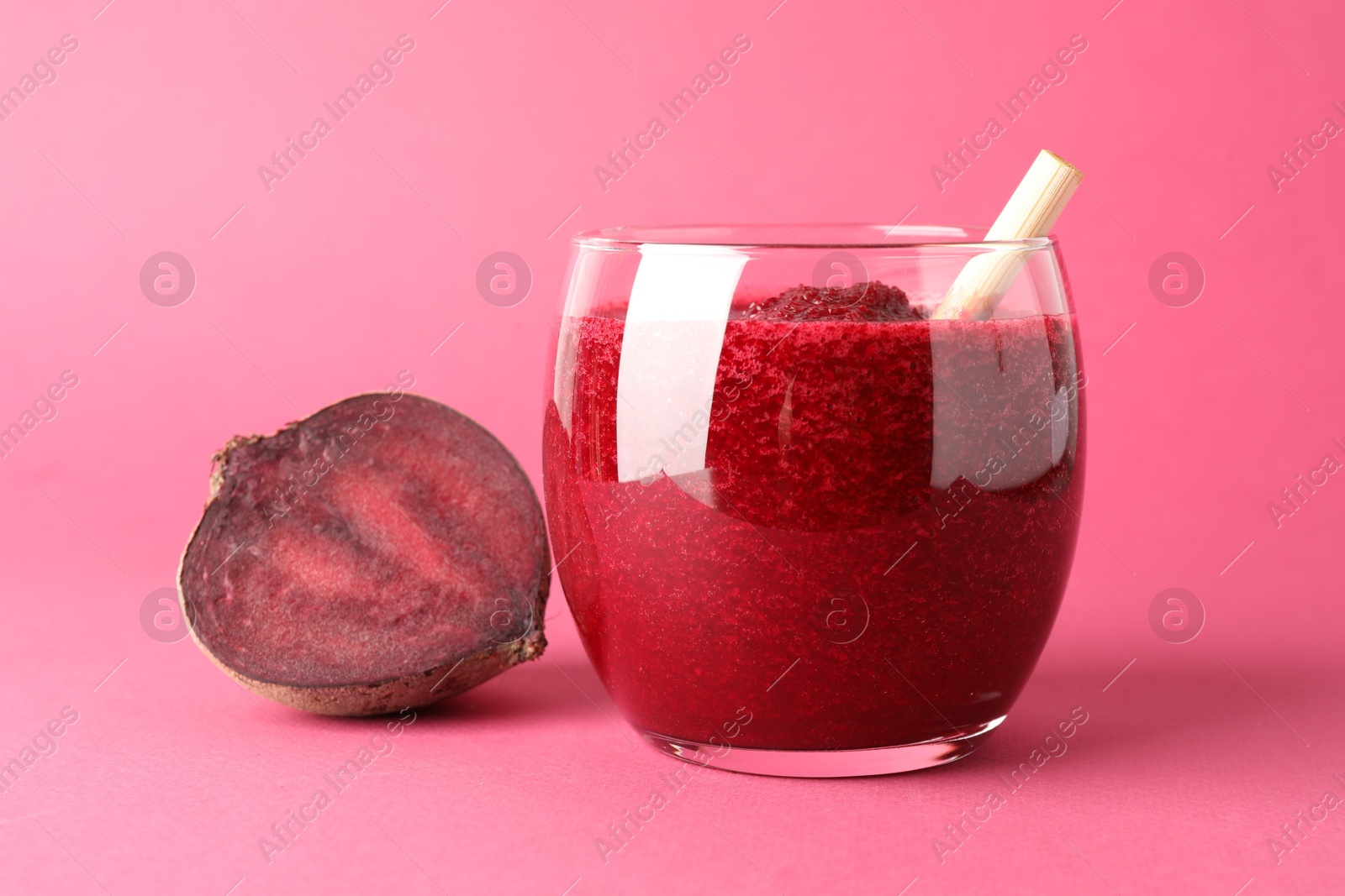 Photo of Fresh beetroot smoothie in glass and half of vegetable on pink background, closeup