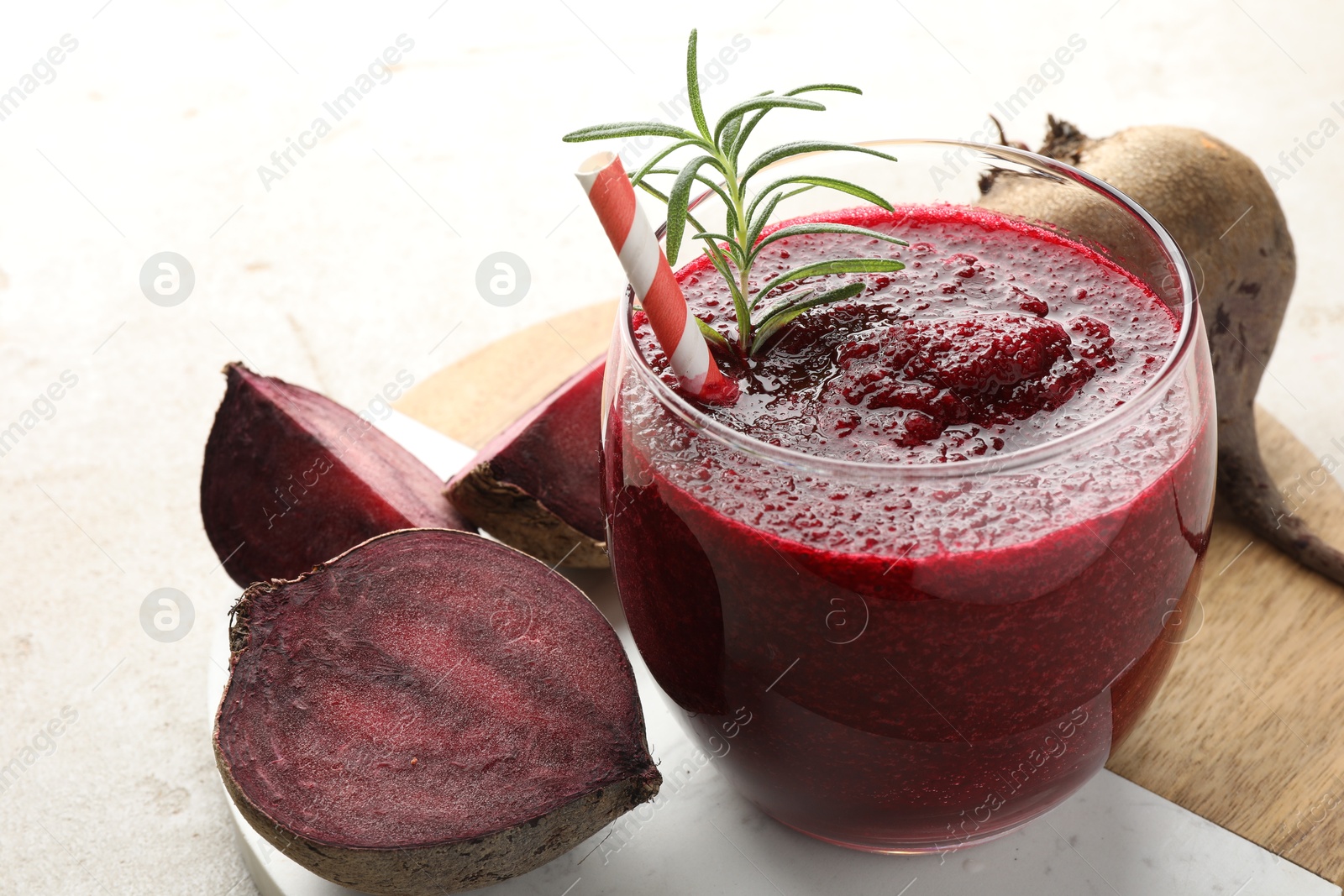 Photo of Fresh beetroot smoothie with rosemary in glass and cut vegetable on light table, closeup