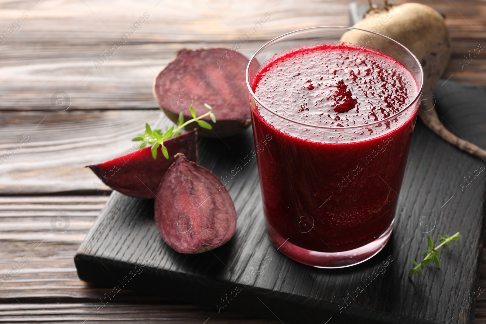 Photo of Fresh beetroot smoothie in glass and cut vegetable on wooden table, closeup