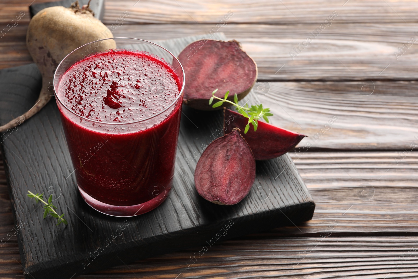 Photo of Fresh beetroot smoothie in glass and cut vegetable on wooden table, closeup