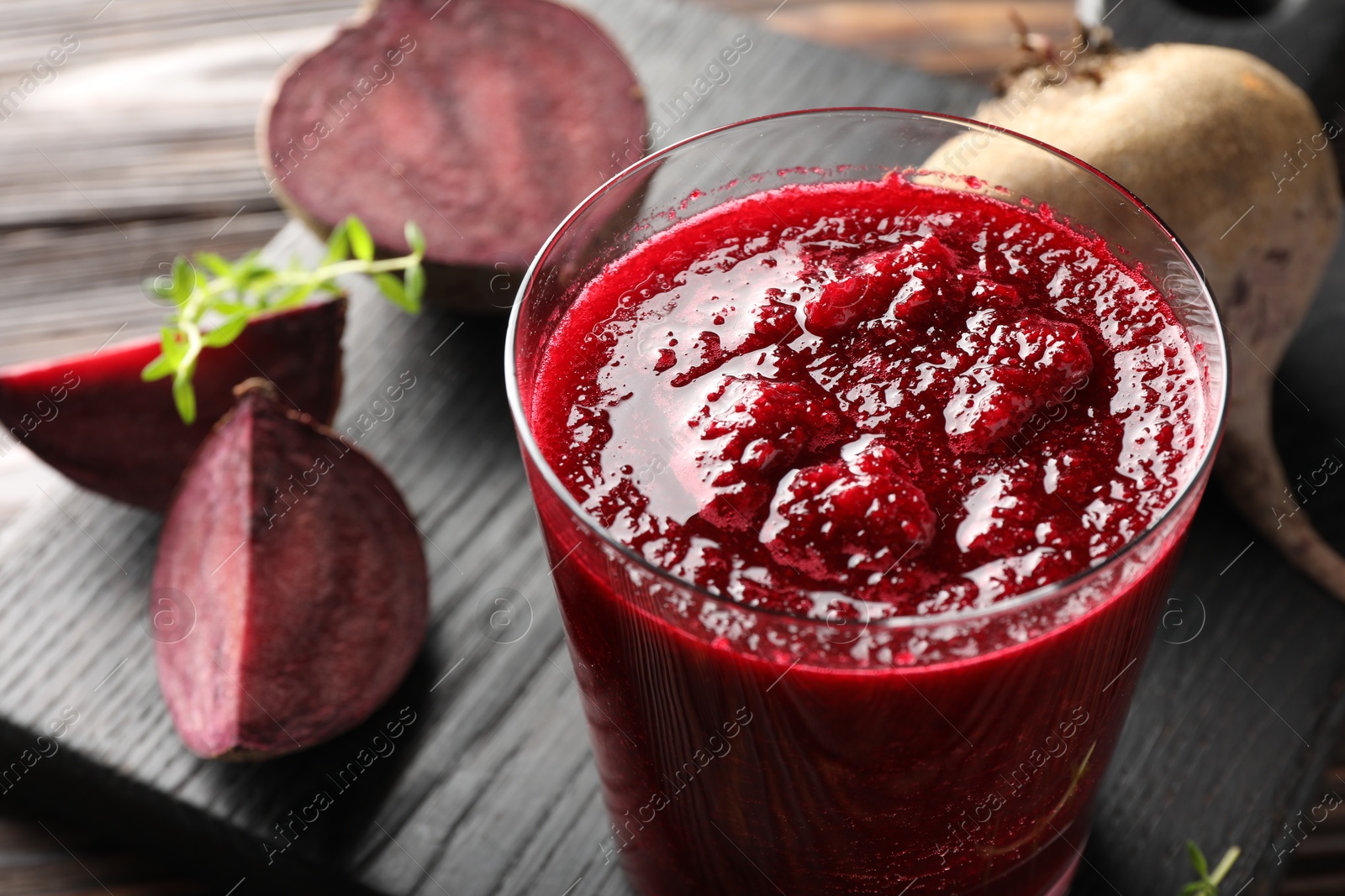 Photo of Board with fresh beetroot smoothie in glass and cut vegetables on wooden table, closeup