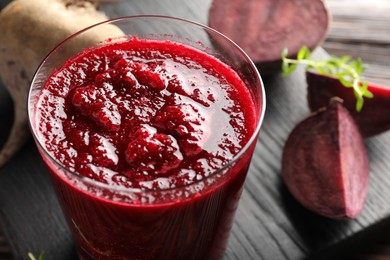 Photo of Board with fresh beetroot smoothie in glass and cut vegetables on wooden table, closeup