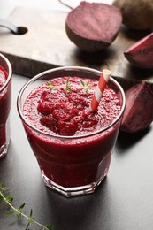 Photo of Fresh beetroot smoothie in glass and cut vegetables on grey textured table, closeup