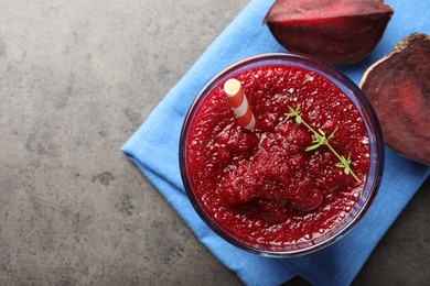 Photo of Fresh beetroot smoothie with thyme in glass and cut vegetable on grey textured table, top view. Space for text