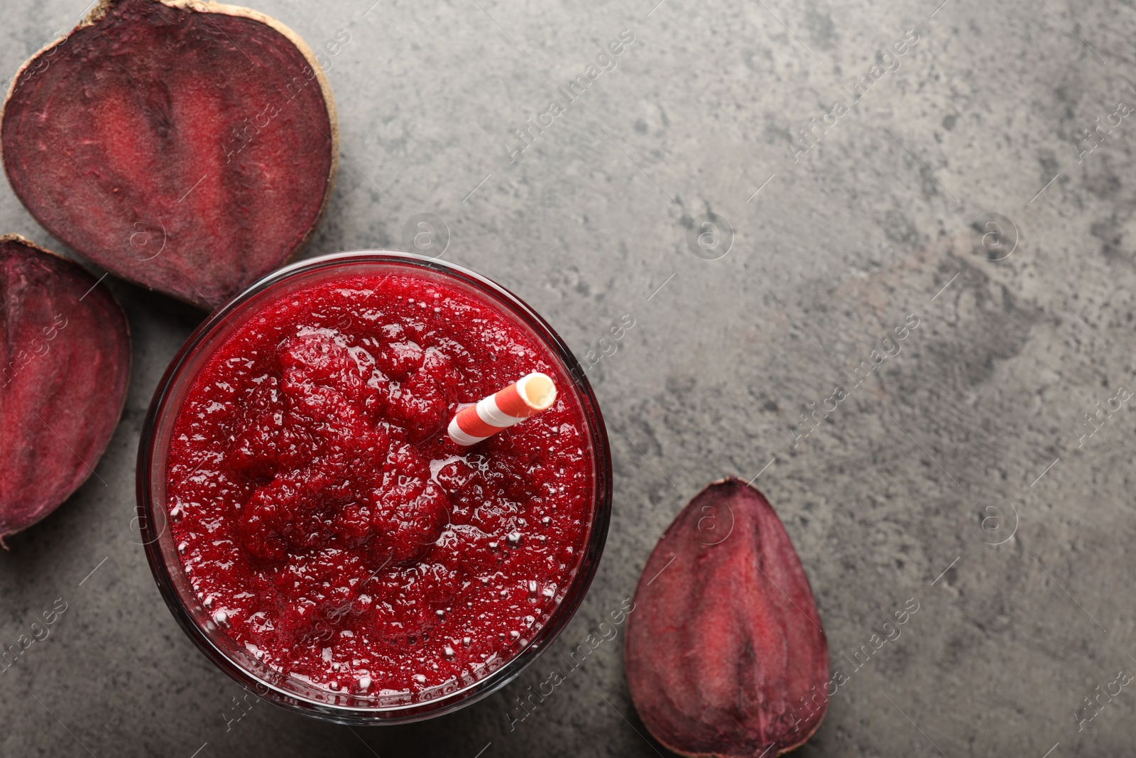 Photo of Fresh beetroot smoothie in glass and cut vegetable on grey textured table, flat lay. Space for text