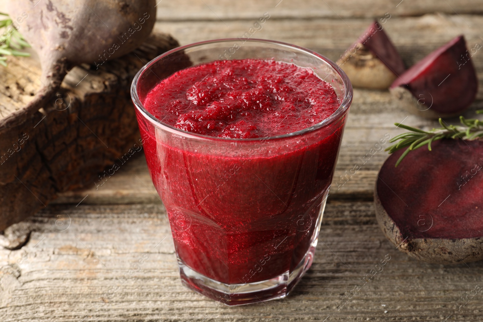 Photo of Fresh beetroot smoothie in glass, rosemary and cut vegetables on wooden table, closeup