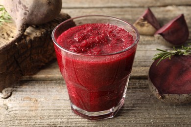 Photo of Fresh beetroot smoothie in glass, rosemary and cut vegetables on wooden table, closeup