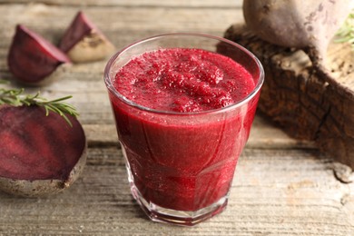 Photo of Fresh beetroot smoothie in glass, rosemary and cut vegetables on wooden table, closeup