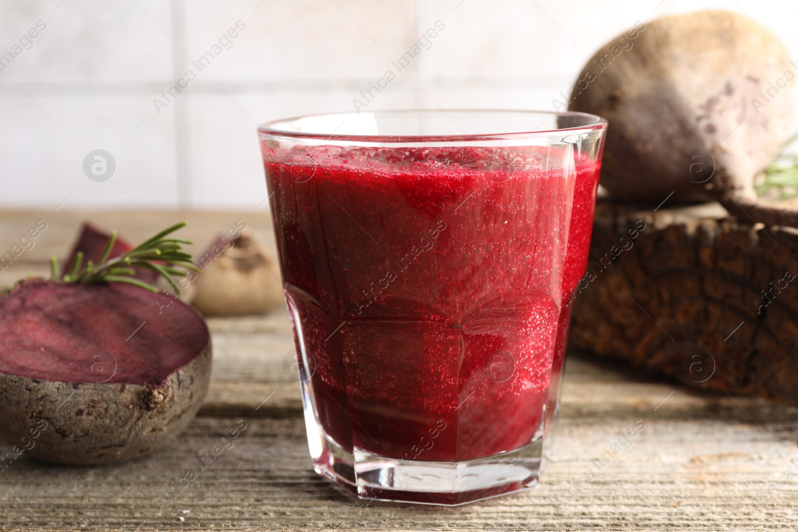 Photo of Fresh beetroot smoothie in glass, rosemary and cut vegetables on wooden table, closeup