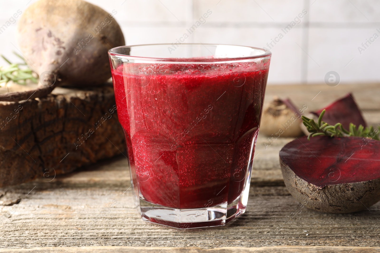 Photo of Fresh beetroot smoothie in glass, rosemary and cut vegetables on wooden table, closeup