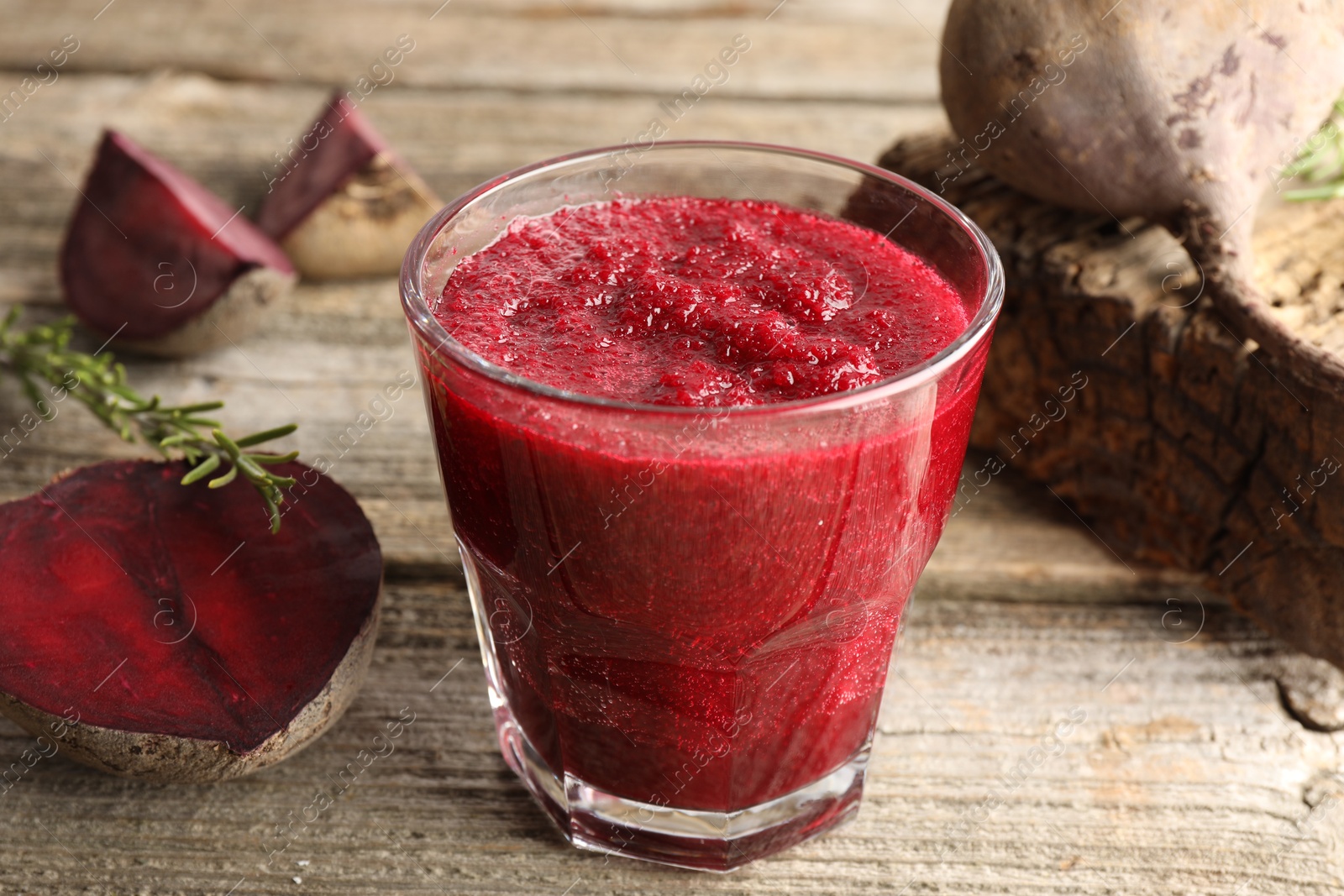 Photo of Fresh beetroot smoothie in glass, rosemary and cut vegetables on wooden table, closeup